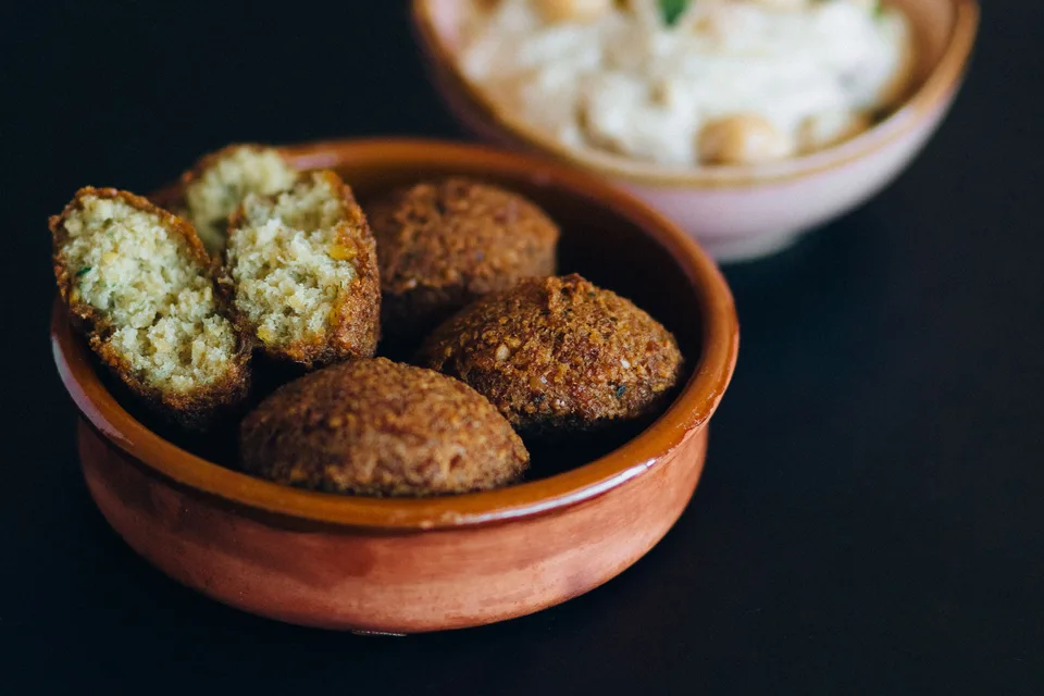 BookNoFees: Fotografie ilustrativă: Biluțe de falafel, inclusiv una tăiată, într-un bol, cu hummus în fundal