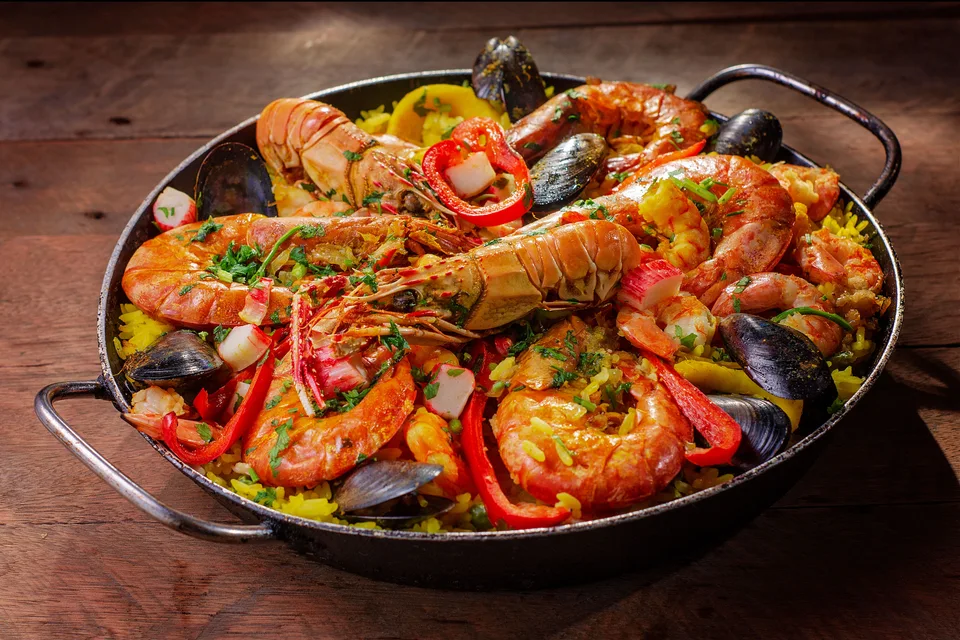 BookNoFees: Fotografie ilustrativă: Paella cu fructe de mare într-o tigaie, acoperită cu crustacee, moluște și ardei roșu