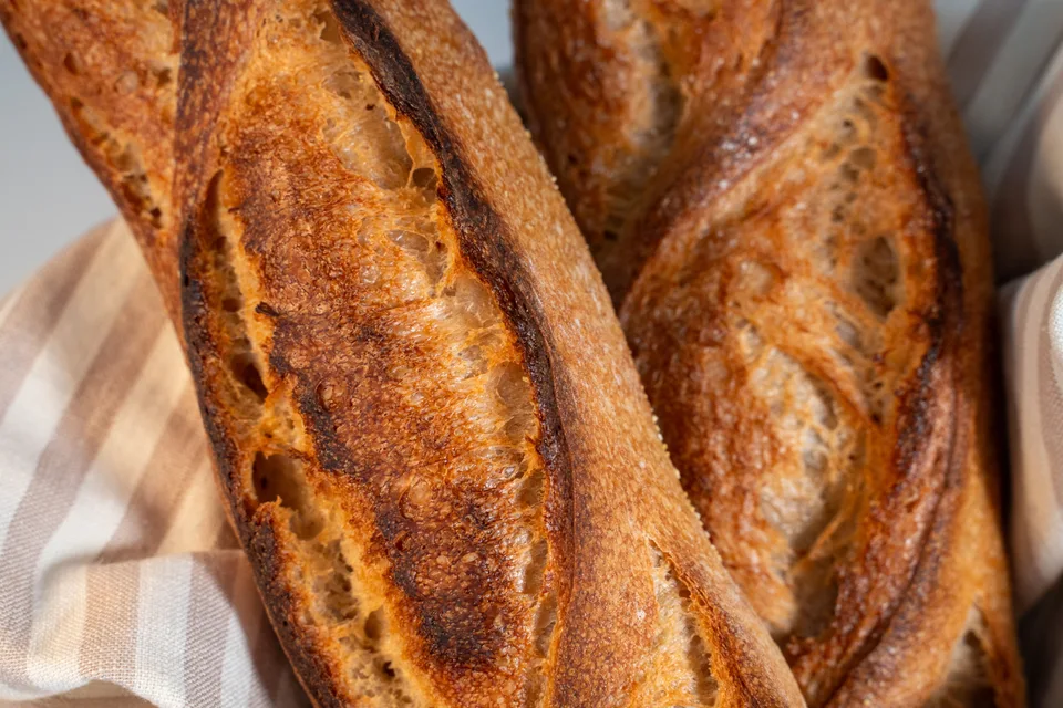Example photo: Golden-brown baguettes resting on a checked cloth